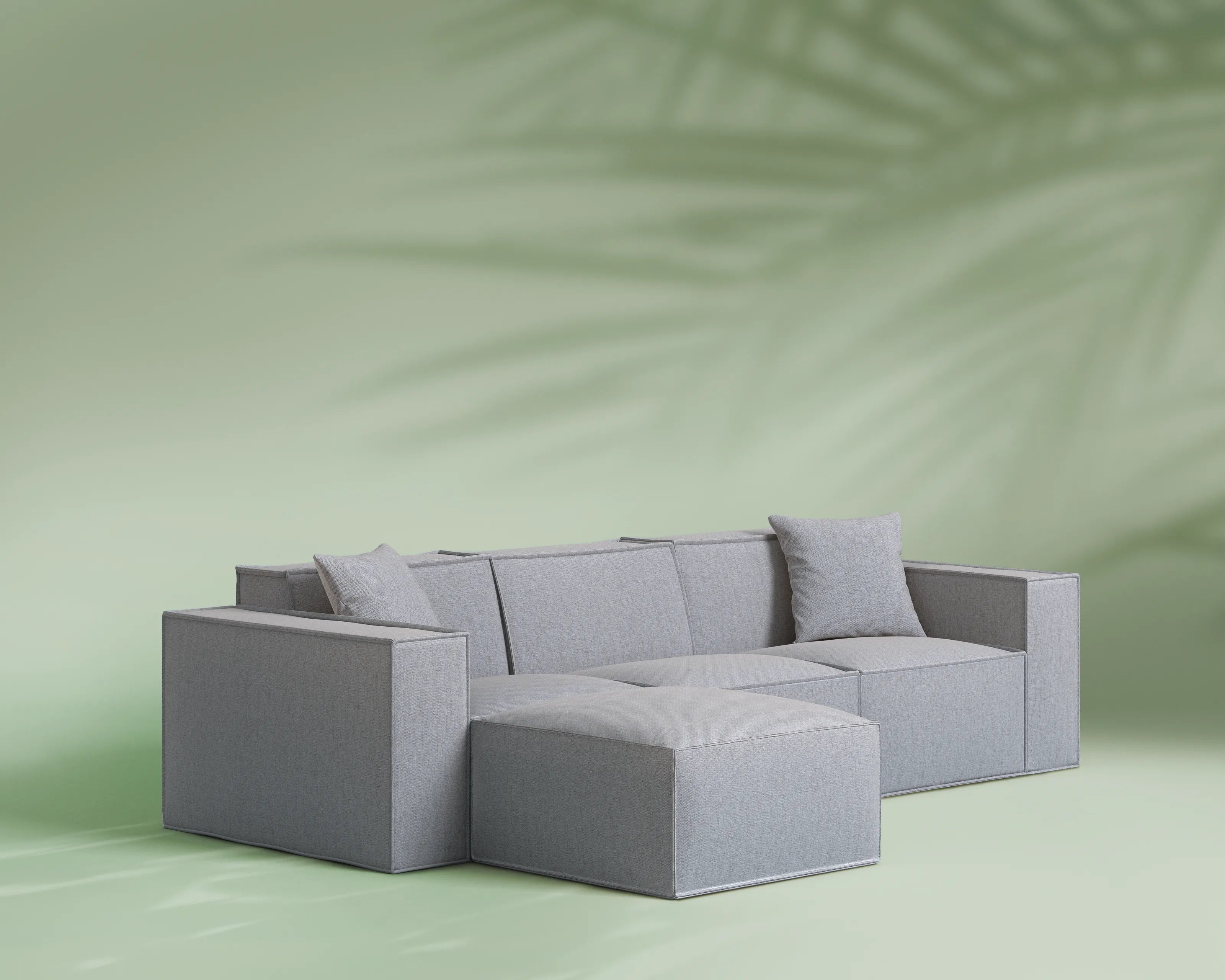 Gray sectional sofa on a light green background with a palm leaf shadow.