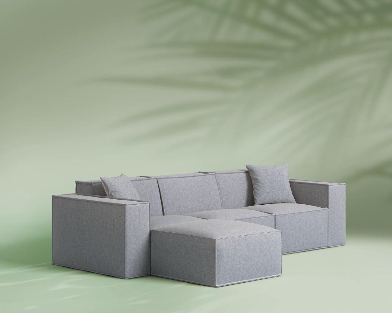 Gray sectional sofa on a light green background with a palm leaf shadow.